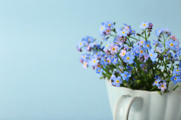 Forget-me-nots flowers in cup, on blue background