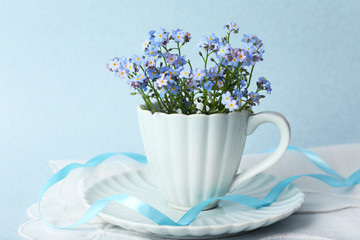 Forget-me-nots flowers in cup, on blue background
