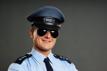 Portrait of smiling policeman in sunglasses on the gray background