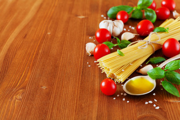 Uncooked spaghetti, cherry tomato, basil, garlic and olive oil, ingredients for cooking pasta, food background, selective focus