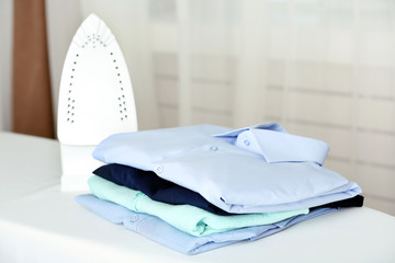 Pile of clothes and electric iron on fabric background