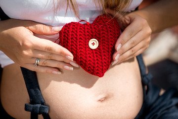 Closeup of young pregnant woman holding red heart on abdomen