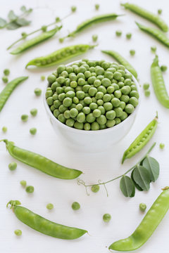Green peas in white bowl on wooden background