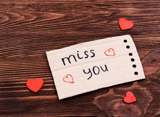 Inscription MISS YOU on cutout carton on wooden background