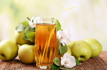 Glass of apple juice and apples on wooden table, on nature background