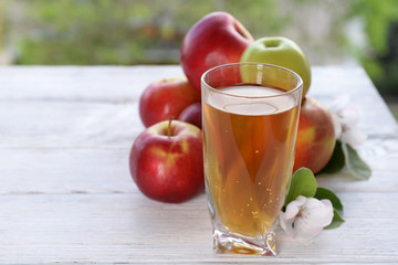 Glass of apple juice and apples on wooden table, on nature background