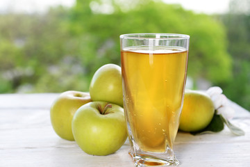 Glass of apple juice and apples on wooden table, on nature background
