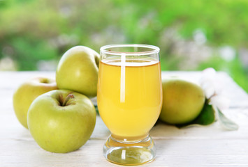 Glass of apple juice and apples on wooden table, on nature background