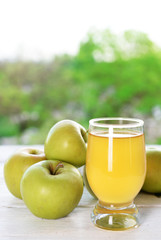 Glass of apple juice and apples on wooden table, on nature background