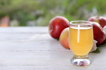 Glass of apple juice and apples on wooden table, on nature background