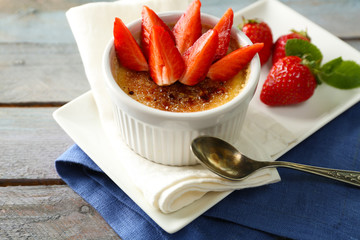 Creme brulee dessert with fresh strawberry berries on napkin, on color wooden background