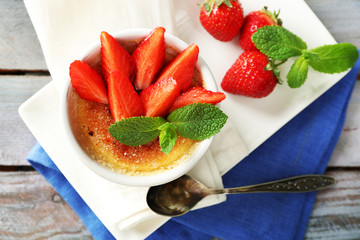 Creme brulee dessert with fresh strawberry berries on napkin, on color wooden background