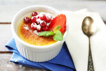 Creme brulee dessert with fresh strawberry berries on napkin, on color wooden background