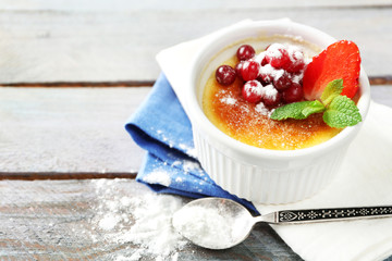 Creme brulee dessert with fresh strawberry berries on napkin, on color wooden background