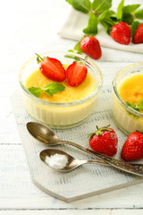 Creme brulee dessert with fresh strawberries and mint leaves, on color wooden background