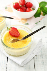 Creme brulee dessert with fresh strawberries and mint leaves, on color wooden background