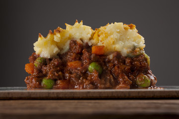 Shepherds pie shot front on on wood with grey background cropped close-up 