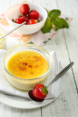 Creme brulee dessert with fresh strawberries and mint leaves, on color wooden background