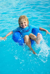 Fototapeta na wymiar Happy little boy with blue life ring has fun in the swimming pool