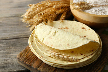 Stack of homemade whole wheat flour tortilla on cutting board, on wooden table background