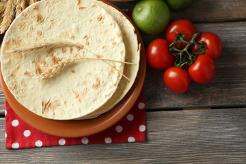 Stack of homemade whole wheat flour tortilla and vegetables on plate, on wooden table background