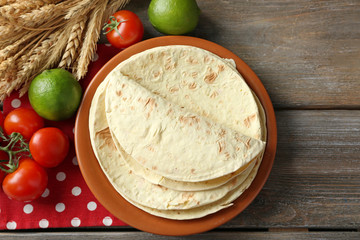 Stack of homemade whole wheat flour tortilla and vegetables on plate, on wooden table background