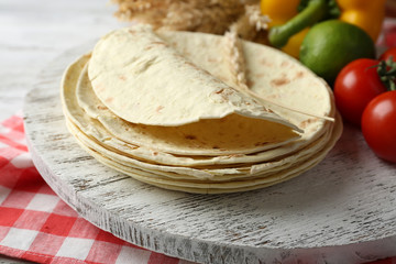 Stack of homemade whole wheat flour tortilla and vegetables on cutting board, on wooden table background