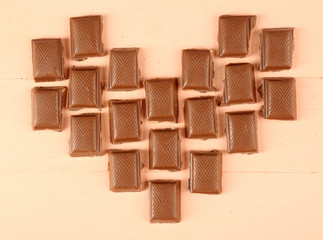 Chocolate pieces arranged in heart shape on light background