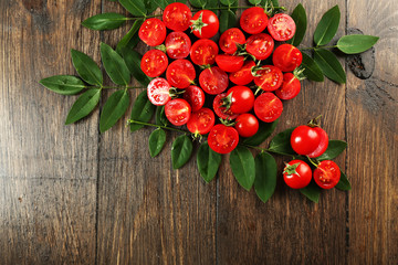 Fototapeta na wymiar Cherry tomatoes arranged in heart shape with green leaves on wooden background