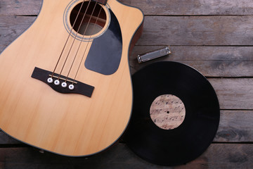 Guitar with vinyl record and harmonica on wooden table close up