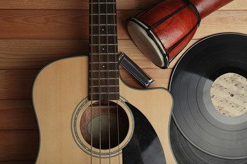 Guitar with vinyl records and African drum on wooden table close up