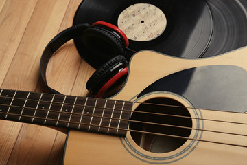 Guitar with vinyl records and headphones on wooden table close up