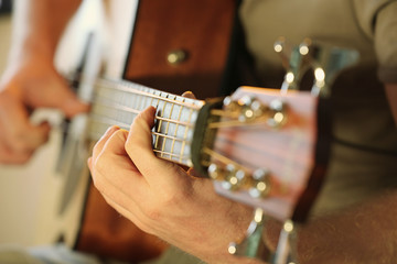 Young man playing on acoustic guitar close up