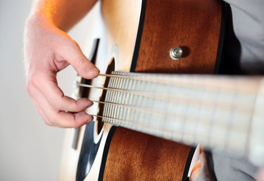 Young man playing on acoustic guitar close up
