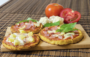 Fototapeta na wymiar Three small round baked pizzas made of cauliflower crust and topped with bacon,ham,halloumi cheese,cottage,lountza,pineapple,turkey,tomato sauce,basil on a wooden chopping board. A healthy pizza snack