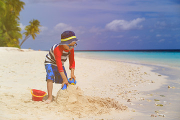 Fototapeta na wymiar little boy building sandcastle on tropical beach