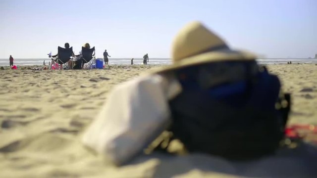 Close up of travel bad with hat on top sitting in the sand on the beach
