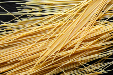 Dry spaghetti pasta on black textured wood from above.