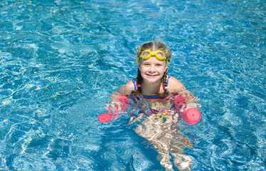 Adorable little girl swimming with a pink foam noodle in a pool
