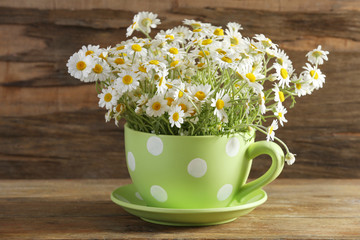 Beautiful bouquet of daisies in cup on wooden background