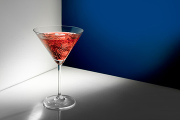 Glass of red martini with ice on the white-blue background