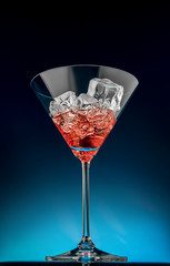Glass of red martini with ice on a blue background