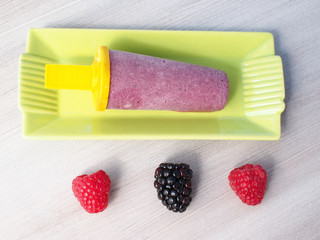 Home made ice cream popsicle with raspberries and blackberries on pastel wooden background