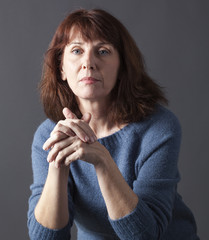 portrait of mature woman with brown hair and blue winter sweater thinking,hands together,looking calm and thoughtful