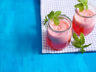 Fresh strawberry and watermelon smoothie decorated with mint on checkered table cloth and blue wooden background