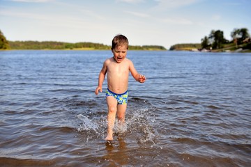 Little cute boy plays in water sunny day in lake