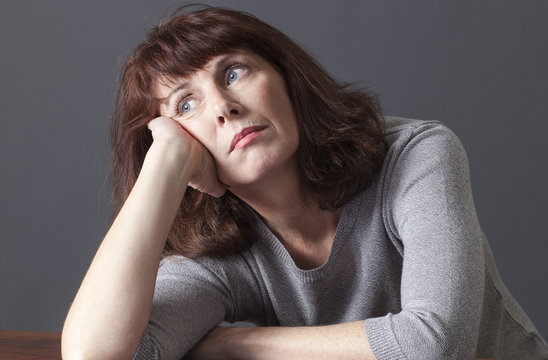 depressed mature woman with brown hair and grey winter sweater leaning her face on hand,looking lost for emptiness