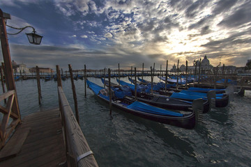 Venice's Santa Maria della Salute sunset view with row of gondola boats in foreground and Santa Maria della Salute.