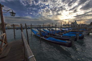 Fototapeta premium Venice's Santa Maria della Salute sunset view with row of gondola boats in foreground and Santa Maria della Salute.