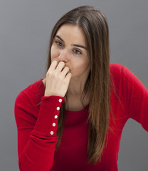 concerned young girl with long brown hair and smart red sweater looking down with hand hiding mouth for unhappiness 